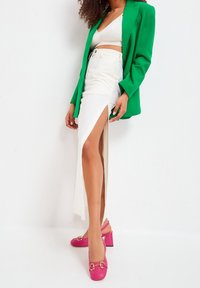 Grön blazer, vit kjol med en hög slits vid låret och rosa klackskor med guldaccenter. Texturerat tyg genomgående.
