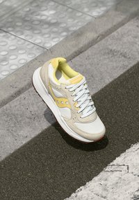 Beige and white sneakers with yellow accents, mesh and leather materials, round toe, textured rubber sole, and white laces.