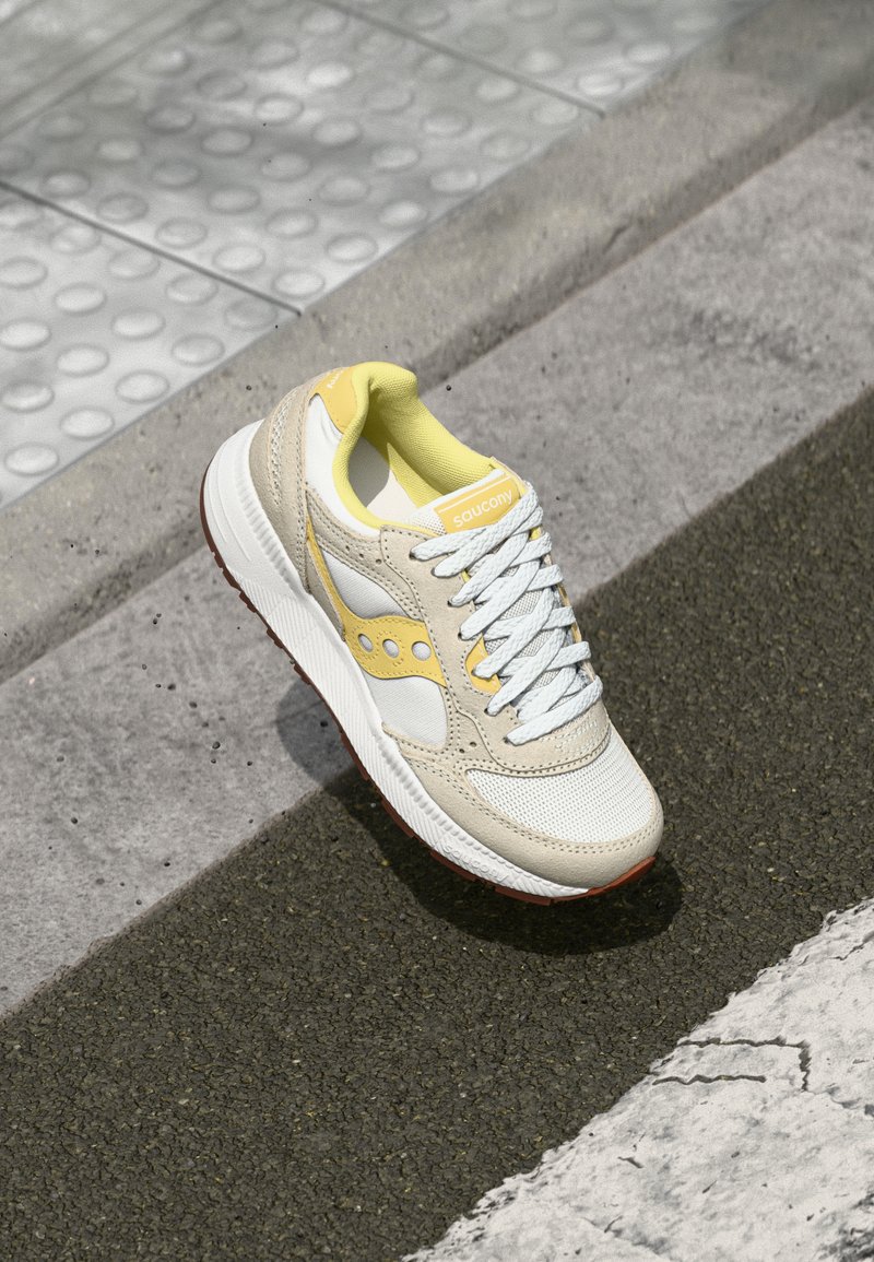 Beige and white sneakers with yellow accents, mesh and leather materials, round toe, textured rubber sole, and white laces.