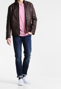 Brun läderjacka med hög krage, bärs över en rosa T-shirt. Matchas med mörk denimjeans och vita sneakers. Slät textur.