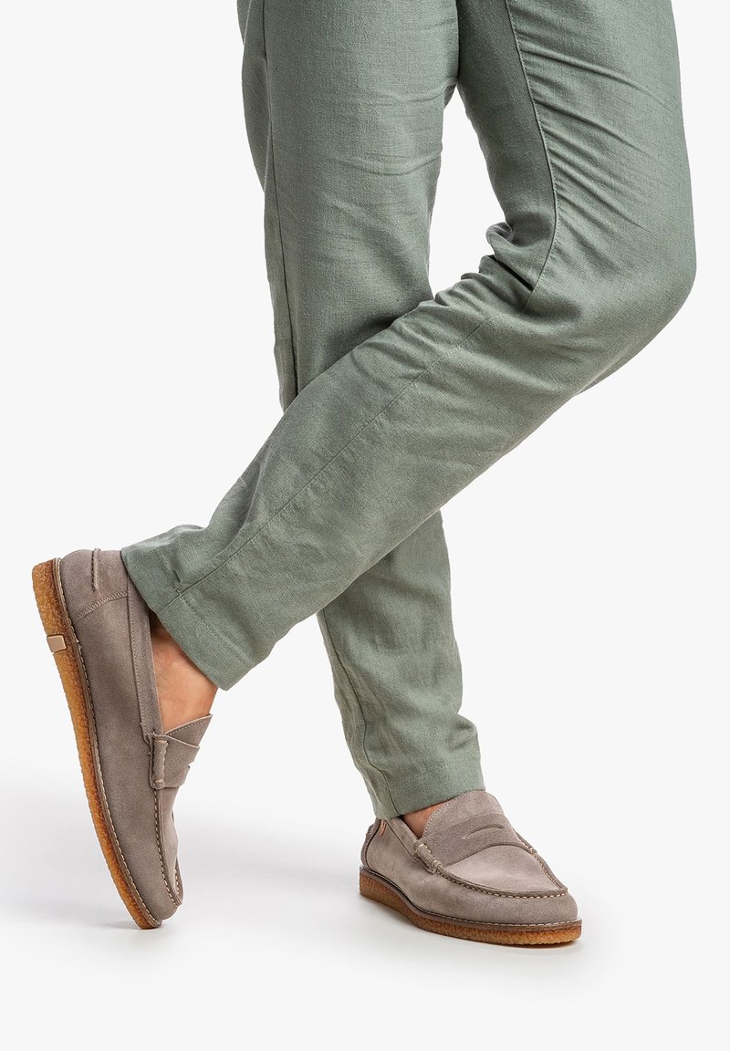 Lys grå ruskindsloafers med en syet design og flad tan gummisål, kombineret med lysegrønne linnedbukser, der viser en afslappet pasform.