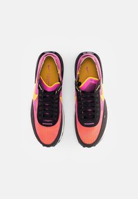 Paire de baskets Nike roses et orange avec des lacets noirs et un swoosh jaune, vues de dessus sur fond blanc.