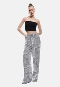 Sort ribbet crop top parret med højtaljede, vide bukser med et monokromt geometrisk mønster og snøre i taljen.