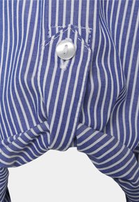 Modrý a bílý pruhovaný materiál s uzlovým detailem. Na levé straně je stříbrný knoflík, který přidává strukturu a texturu tomuto oděvu.