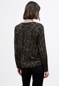 Blusa de manga larga con estampado de leopardo en marrón y negro. Material suave con un ajuste relajado y detalles fruncidos en la parte trasera.