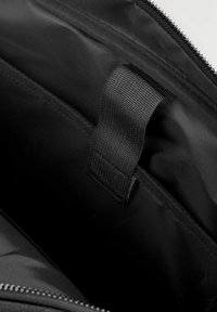 Black fabric bag interior featuring a textured finish, a zippered opening, and a webbing strap for easy access.