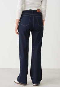 Dark blue wide-leg jeans with a high waist, five pockets, and brown leather label on the back waistband, featuring contrasting stitching.