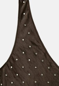 Top de tela marrón con diseño halter, adornado con tachuelas plateadas en forma circular dispuestas en un patrón sobre la superficie.