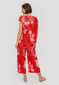 Rode bloemen twee-delige outfit met korte mouwen. Heeft een geplooid ontwerp en wijde broekspijpen, versierd met witte en blauwe patronen.