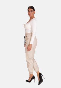Biały top z długim rękawem i okrągłym dekoltem, zestawiony z beżowymi, zwężanymi joggerami z elastycznymi mankietami i sznurkiem w pasie. Czarne szpilki.