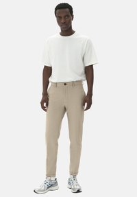 Pantaloni bej croiți, cu o textură netedă, având un închizător cu un singur buton și mansete. Asortați cu un tricou alb simplu cu mânecă scurtă și adidași.