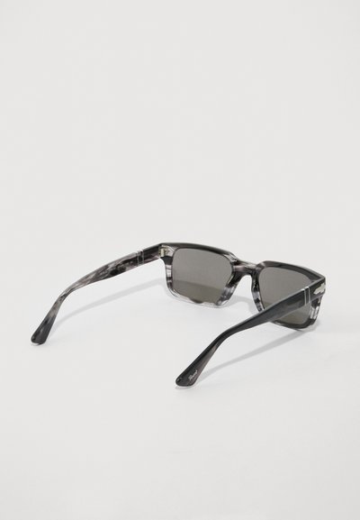 Taisnstūra formas pelēkā tonī brilles ar melnu un pelēku marmora plastmasas rāmjiem, kas atrodas uz baltas virsmas, salocītas vaigu kaulos.