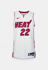 Balts basketbola krekls ar sarkaniem akcentiem, uz kura apakšējiem burtiem rakstīts "HEAT" treknā sarkanā krāsā, zem tā numurs "22", un apakšā ir Nike logo un NBA birka.