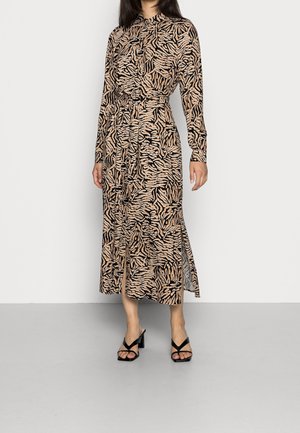 Femme portant une robe à manches longues, boutonnée, ceinturée à imprimé animalier avec une fente midi, associée à des sandales noires à talons.