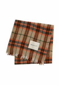 Écharpe en laine beige avec un motif tartan orange, vert et noir. Bords frangés et étiquette en tissu affichant la marque "GANT."