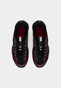 Chaussures de sport noires et rouges avec une tige en tissu texturé, des accents réfléchissants, un col rembourré et un amorti d’air visible dans la semelle.