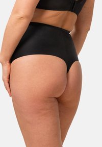 Biancheria intima nera a vita alta realizzata in tessuto liscio, con un design senza cuciture e un aspetto minimalista. Vista posteriore che mostra la vestibilità e la copertura.