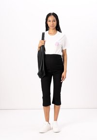 T-shirt blanche avec imprimé floral rose, pantalon noir court, et baskets blanches. Le mannequin porte un sac fourre-tout noir.