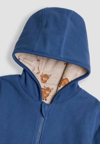 Felpa con zip ribaltata blu, dotata di cappuccio foderato in tessuto beige stampato con piccole illustrazioni di bovini delle Highland marroni.
