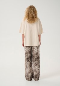 Beżowa, oversize, krótko rękawowa bluzka z okrągłym dekoltem w komplecie z brązowymi, szerokimi spodniami w tie-dye, podkreślająca miękki, teksturowany materiał.