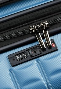 Blauwe harde koffer met verticale ribbels, voorzien van een zwarte rits met dubbele trekbanden, een TSA-combinatieslot en een beveiligingslogo.