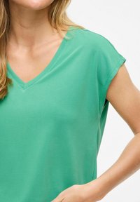 Camiseta verde de cuello en V con mangas cortas, hecha de una tela suave y lisa. Presenta un corte relajado y un diseño simple y limpio.