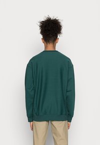 Sweatshirt em azul-água com decote redondo e mangas longas, apresentando uma bainha e punhos canelados; textura suave, ajuste casual.