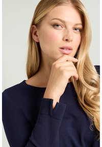 Maglione blu navy con scollo rotondo e polsini testurizzati, caratterizzato da uno speciale dettaglio a spacco. Tessuto liscio con design aderente.