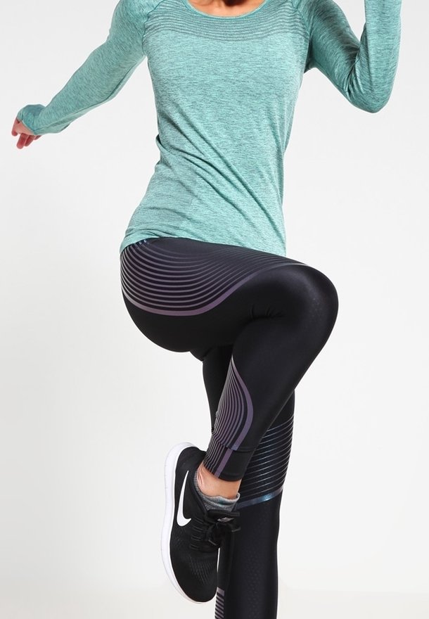 Jasnozielona, długorękawowa koszulka sportowa w połączeniu z czarnymi legginsami z fioletowymi poziomymi paskami. Czarne buty sportowe dopełniają cały strój.