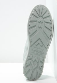 Světle šedá podrážka tenisky s texturovanou gumou pro lepší přilnavost. Obsahuje geometrické vzory na podrážce a branding. Materiál se zdá být syntetický s matným povrchem.