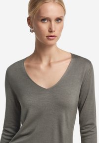 Grå långärmad V-ringad tröja i mjukt material, med en slät textur och en figurnära design.