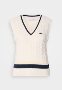 Ärmelloser, cremiger Kabelstrickpullover mit V-Ausschnitt, marineblauen Akzenten und einem grünen gestickten Logo auf der Brust. Besitzt gerippte Details.