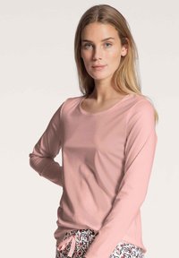 Long-sleeve t-shirt in soft pink fabric with a rounded neckline. Features a relaxed fit and is paired with patterned pajama pants.