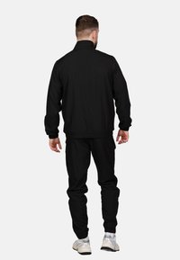 Schwarze Jacke mit Reißverschluss, hochgeschlossenem Kragen, elastischen Bündchen und lockerer Passform, kombiniert mit passenden Hosen und silbernen Sneakern.