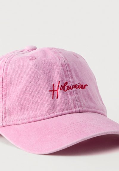 Ροζ καπέλο μπέιζμπολ με κόκκινο κεντημένο λογότυπο "Holzweiler" στο μπροστινό πάνελ, εμφανίζεται σε λευκό φόντο.