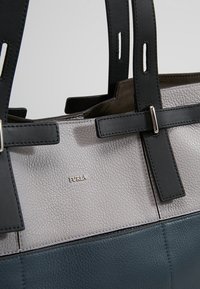 Primo piano di una borsa a tracolla in pelle con texture bicolore, dotata di manici neri regolabili e logo Furla in argento sul pannello superiore grigio.