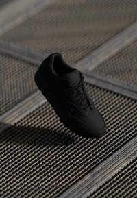 Sorte sneakers med en glatt læroverdel, rund tå og flate lisser. Har en teksturert såle og subtil merkingen på tungen.