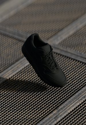 Baskets noires avec une tige en cuir lisse, bout rond et lacets plats. Présente une semelle texturée et un branding discret sur la languette.