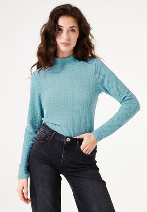 Lichtblauw, gestructureerd langemouwen top met hoge hals, gecombineerd met zwarte jeans met knoopsluiting en zakken.