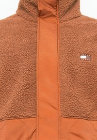 Brown fleece jacket featuring a smooth, contrasting orange front panel, a high collar, and a small Tommy Jeans logo on the chest.