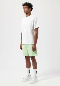 Bílý bavlněný tričko, mátově zelené kraťasy, bílé tenisky a vzorované bílé ponožky. Obsahuje akcenty loga na kraťasech a ponožkách.