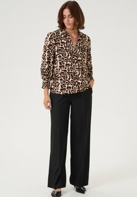 Leopard print blouse with a button-down front, long sleeves with gathered cuffs, paired with wide-leg black trousers and pointed black shoes.