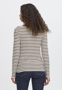 Brun og creme stribet langærmet top, ribbet tekstur, rund halsudskæring, med tætsiddende design og en lige kant. Parret med mørke jeans.