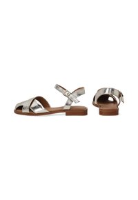 Metallische zilveren platte sandalen met kruislings gespen, enkelgesp detail, open teen en een gladde tan zool.