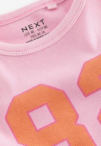 Różowa, prążkowana koszulka T-shirt z nadrukiem w kolorze pomarańczowym i różowym, z numerem 88. Dekolt ozdobiony metką z instrukcjami pielęgnacji i informacjami o marce.