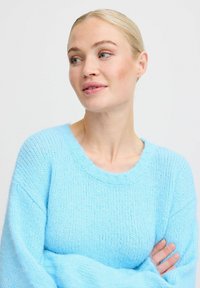 Pullover lavorato a maglia di un blu chiaro, dal vestibilità ampia, con scollo rotondo e maniche lunghe. Tessuto morbido con una finitura leggermente pelosa.