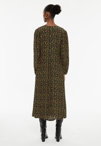 Zwarte bloemenjurk met gele patronen, lange mouwen en een vloeiende uitstraling, gecombineerd met zwarte kniehoge laarzen. Glad fabrieksweefsel.
