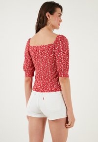 Red floral print top with short puff sleeves and a square neckline, made of lightweight fabric, paired with white denim shorts.