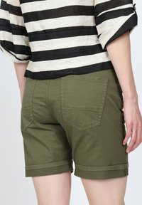 Olivgröna shorts med uppvikta kanter, gjorda av bomullstyg, med två bakfickor och synlig sömdetalj. Randig svart och vit topp.