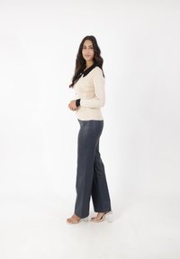 Cardigan de canalé marfil con cuello y botones negros, combinado con pantalones de talle alto azul oscuro; sandalias de tacón cuadrado transparentes completan el look.